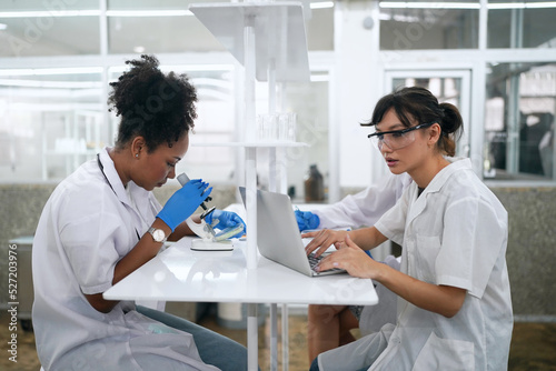 Young scientist in white lab coat working with binocular microscope in the material science lab