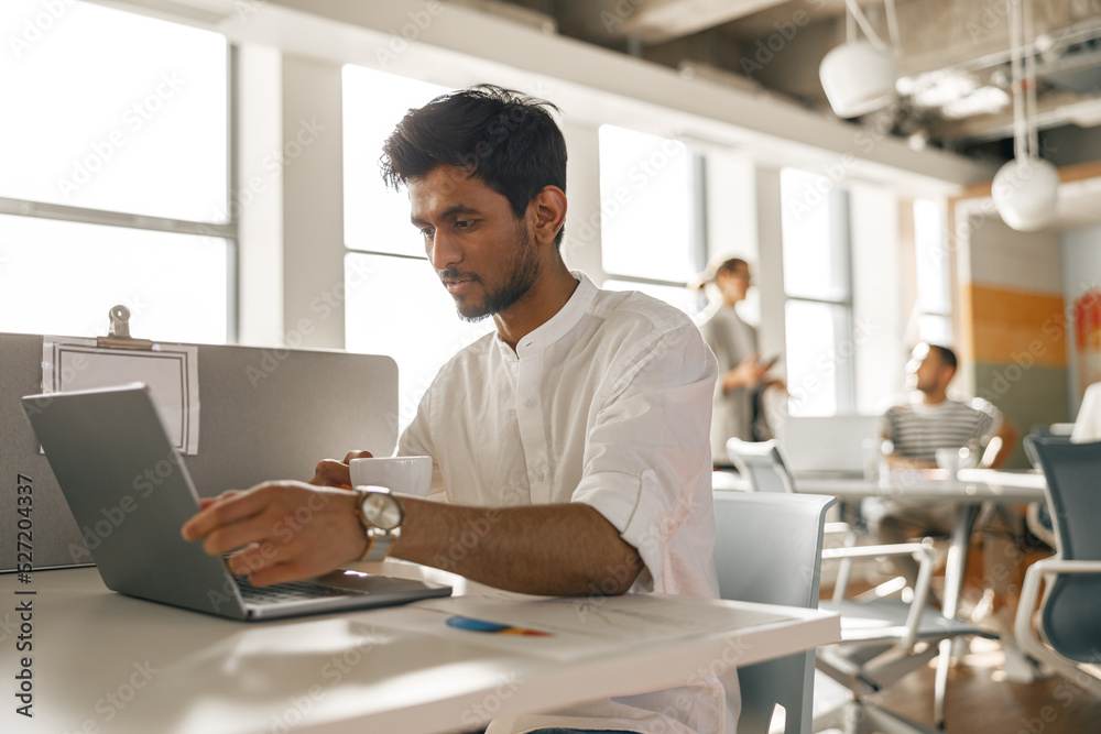 Businessman working laptop while sitting in modern office on colleagues background