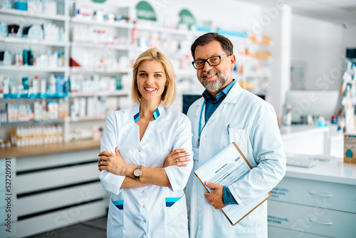 Portrait of confident pharmacist and her mature coworker in pharmacy and looking at camera. photo