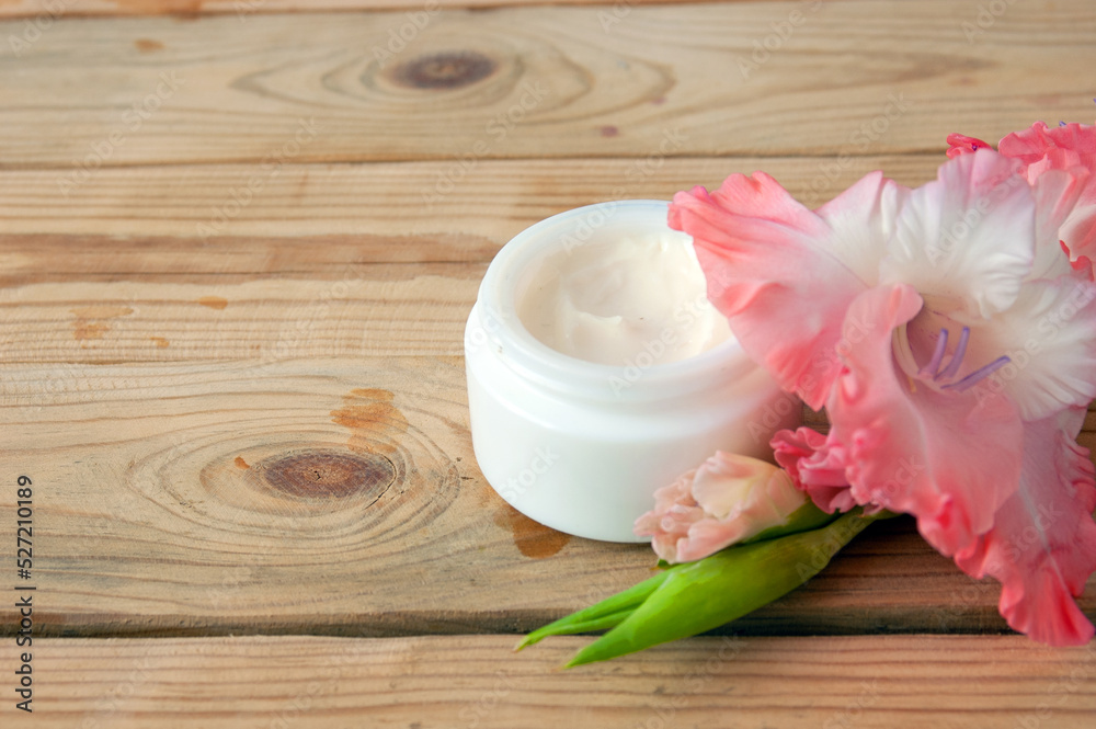 cosmetic cream and gladiolus flowers bunch on wooden background. Organic cosmetic concept. Natural cosmetic cream with flower extract
