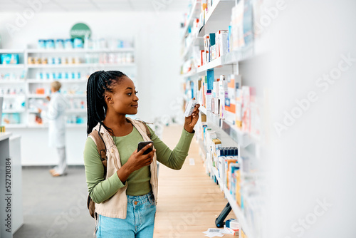 Young black woman using cell phone while looking for medicine in pharmacy. photo