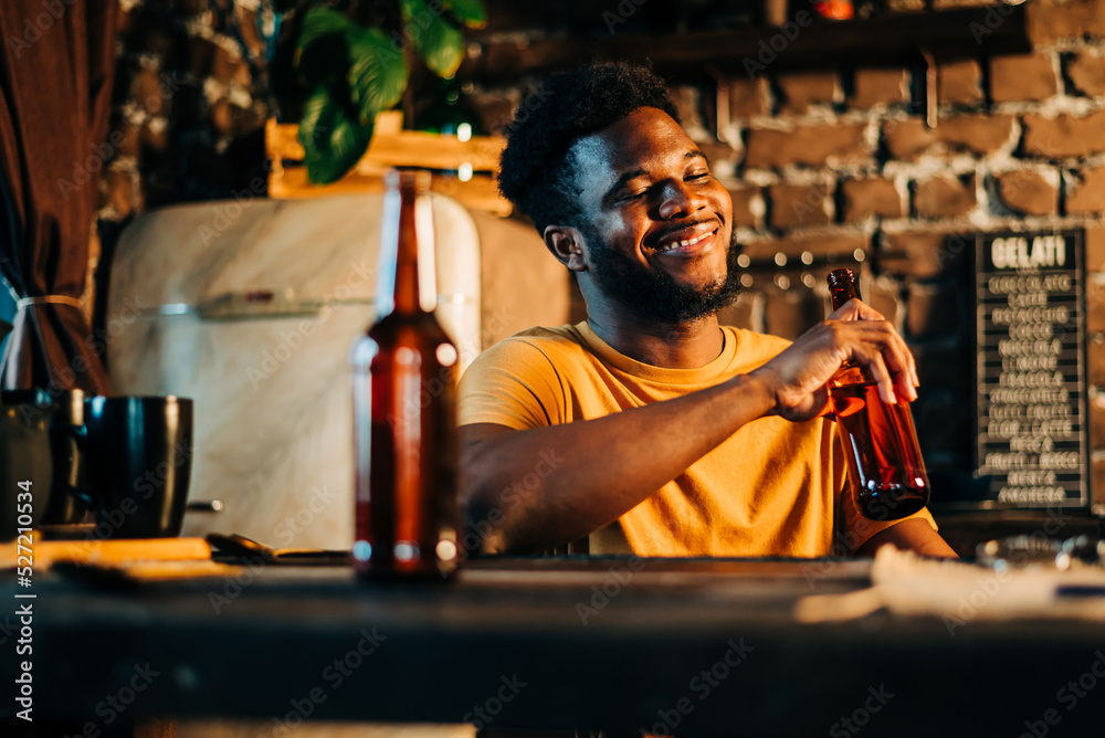 Φωτογραφία Shot of attractive african young happy smiling man drinking beer bottle in the bar close up portrait