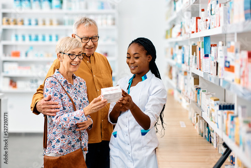 Happy black female pharmacist assists senior couple in choosing medicine in pharmacy.