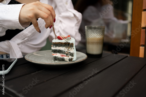 Woman eating a piece of cake and cup of latte coffee in outodoor cafe of city. photo