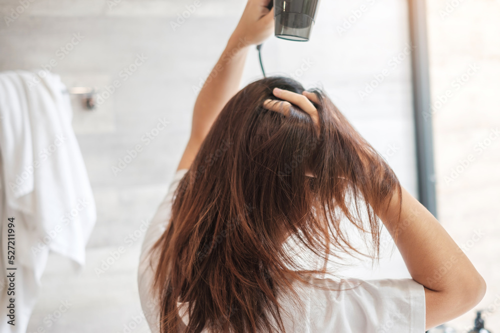 Naklejka premium young woman using hair dryer at home or hotel. Hairstyles and lifestyle concepts