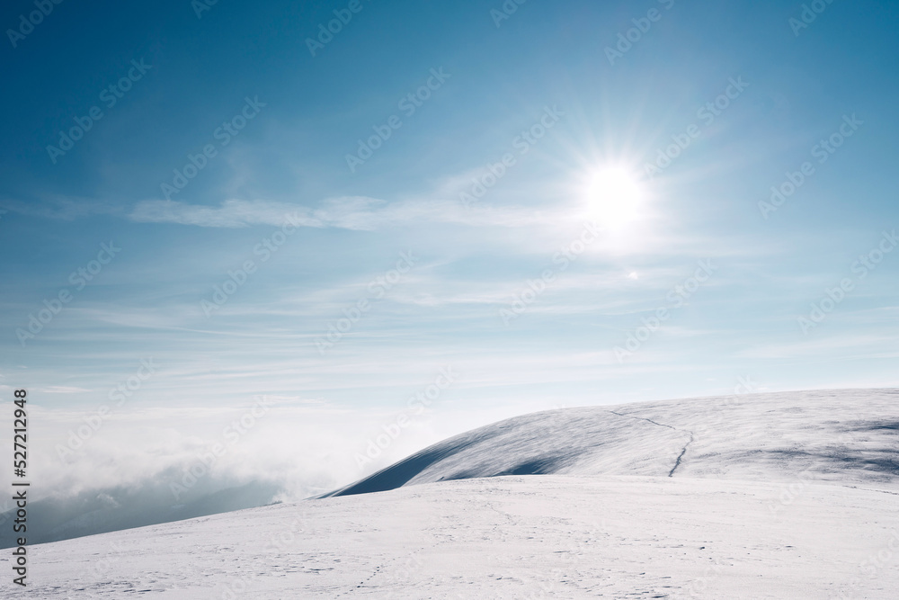 The sun over a snowy mountain slope. A trail running along a snow-covered mountain slope.