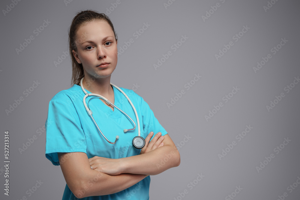 Photo of professional nurse with stethescope dressed in blue uniform posing with crossed arms. Photo of professional nurse with stethescope dressed in blue uniform posing with crossed arms.