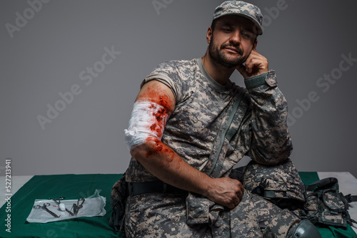 Fototapeta Shot of wounded soldier patient dressed in camouflage uniform looking at camera