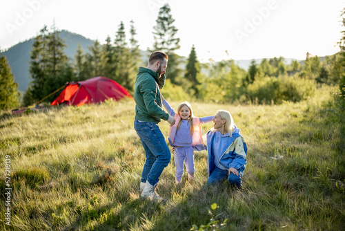 Young caucasian couple with little girl and dog have fun spending leisure time together while travel with tent in the mountains. Happy family summer vacation at campsite