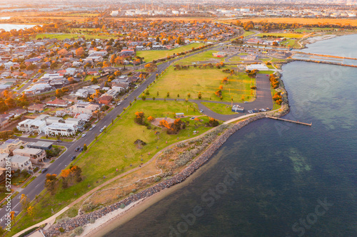 Aerial view of coastal reserve and suburb next to a calm bay at sunset