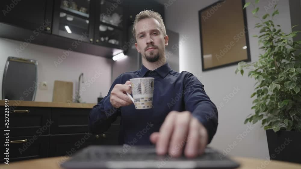 Man cheers with morning coffee while typing one hand on laptop in kitchen 4K Man cheers with morning coffee while typing one hand on laptop in kitchen 4K