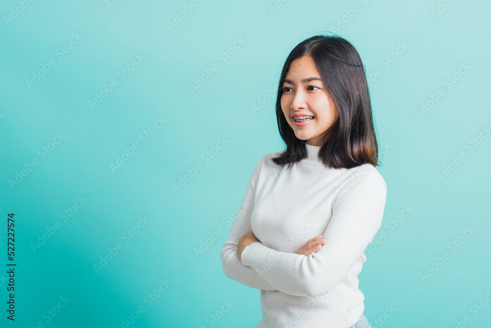 Fototapeta premium Young beautiful Asian woman smiling with crossed arms, Portrait of positive confident female stand cross one's arm, studio shot isolated on a blue background