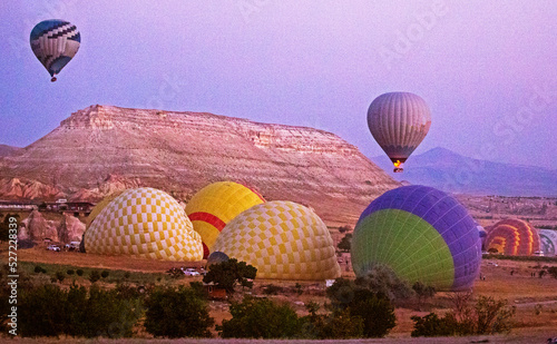 huge hot air balloons with and without flame before flying with bizarre mountain silhouettes in the Cappadocia valley in the early morning.