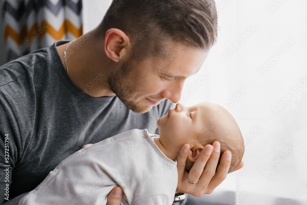 Fototapeta premium Portrait of a young Caucasian father keeping his newborn son at home.