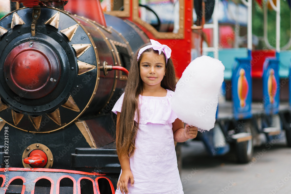 Child girl in an amusement park in the summer eats cotton candy and smiles happily. The concept of summer holidays and school holidays