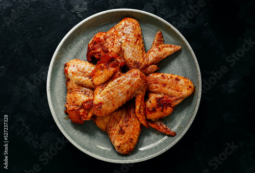 Raw chicken wings marinated in paprika and curry. Copy space. Raw meat in a plate. Dark background, top view. photo