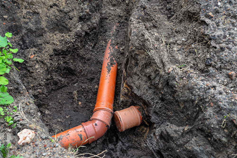 Obraz premium An orange plastic pipe from a septic tank with a diameter of 160 mm lying in a ditch, blind pipe visible.