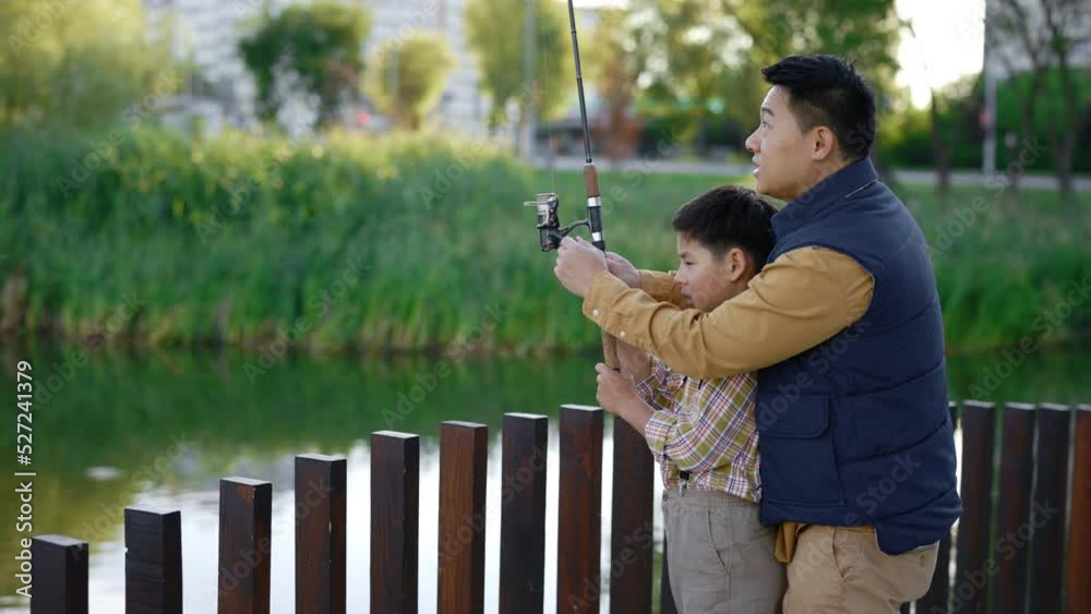 Asian dad shows his son how to cast a fishing rod on practice, gives ...