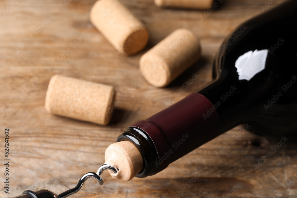 Opening wine bottle with corkscrew on wooden table, closeup