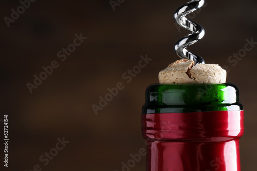 Opening wine bottle with corkscrew on dark brown background, closeup. Space for text