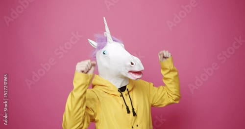 Man with unicorn mask making funny gestures. Man with Unicorn Mask. Fun and happiness concept. Funny Guy in Yellow Suits Dance with Unicorn Mask, Man having fun on isolated pink Background. 