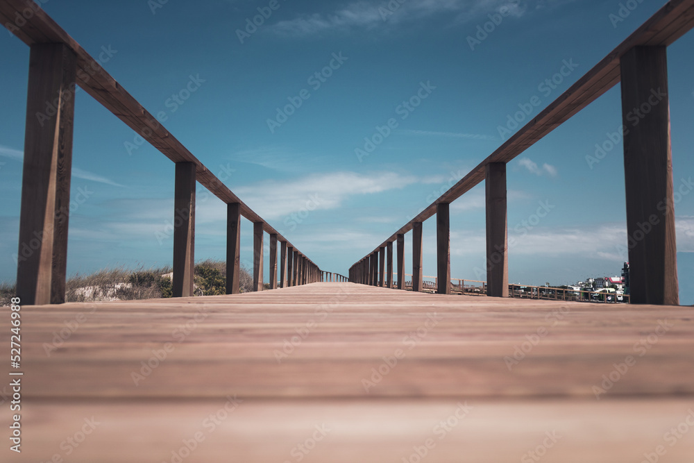 Long wooden pier boardwalk and handrail in Quiaios beach area with low viewpoint perspective and the blue sky above. Leading lines with selective focus and empty space for text