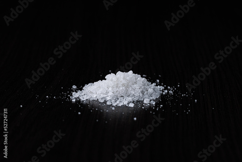A pile of coarse-grained sea salt on a black table background. Selective focus. Close-up.