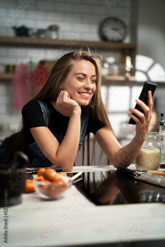 Young woman in kitchen. Beautiful woman using the phone while cooking delicious food