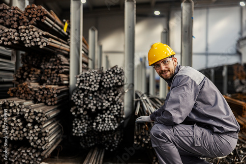 A metallurgy worker is crouching next to iron and metal bars and counting them. Expense of the iron and metal concept. photo