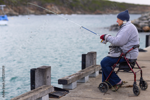 old lady with mobility aid fishing with fishing rod on jetty