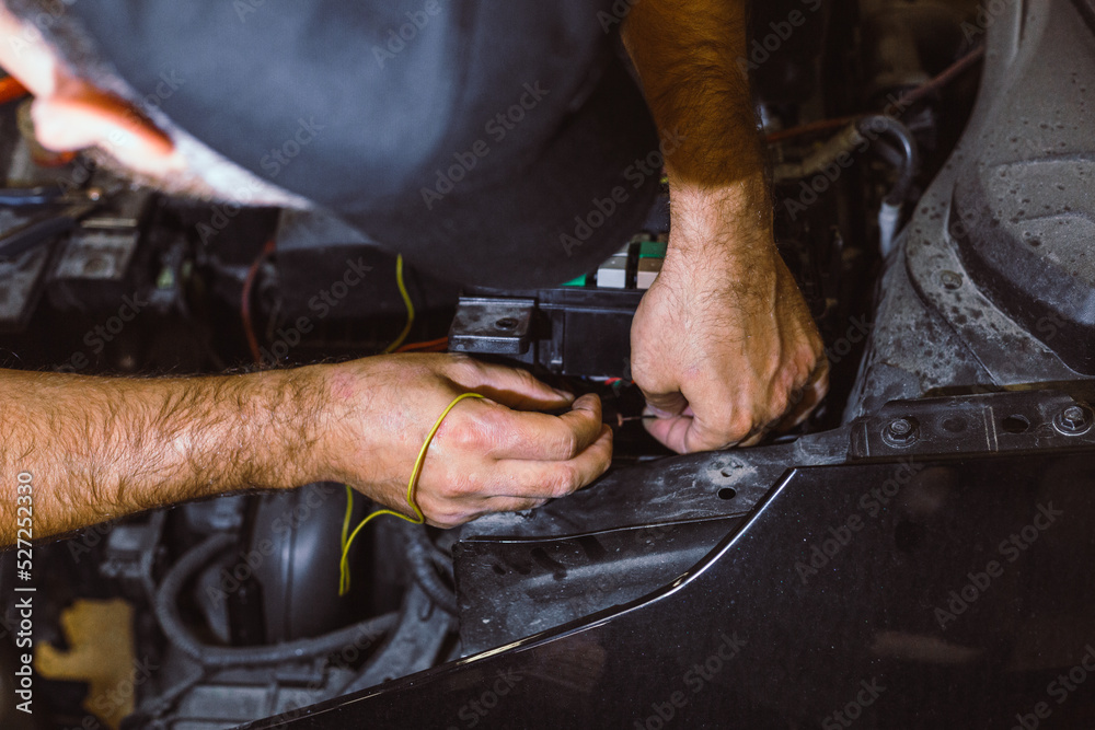 The concept of car service, repair, tuning, maintenance. The car electrician fixes problems in the electronics of the car. Hands of an electrician working with an electrical unit in a car close-up.