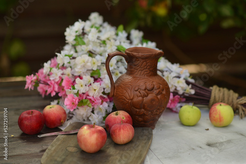 Clay jug, apples on a board and apple blossom on a wooden table, the concept of life outside the city and in the countryside