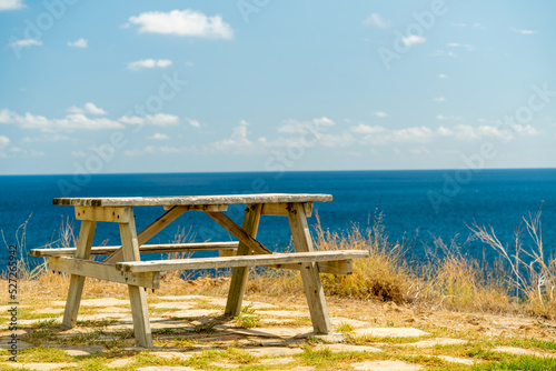 A lonely bench with a table on the edge of a cliff by the sea. Summer sun.