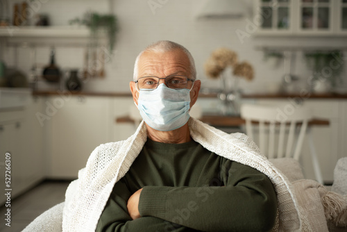 Portrait of an elderly gray-haired man in a protective face mask in a cold winter at home.
