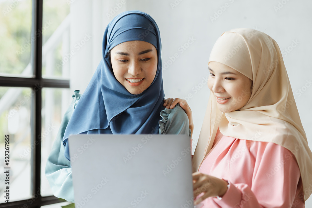 Two hijab-clad Asian women are brainstorming together in a conference room for a startup, run by a young, talented woman. The management concept runs the company of female leaders to grow the company.