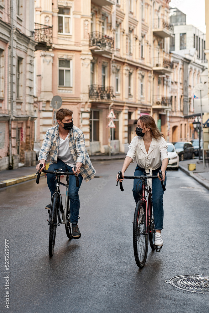 Young caucasian couple wear masks ride bicycles