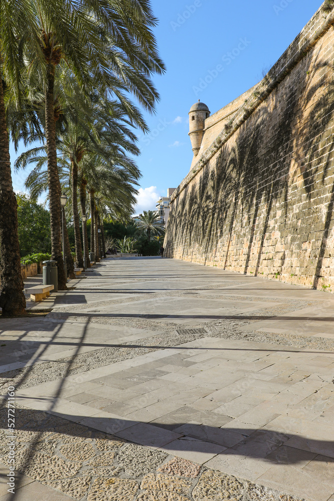 Paseo con palmeras junto a la muralla medieval de Palma de Mallorca, con el bastión en uno de sus extremos.