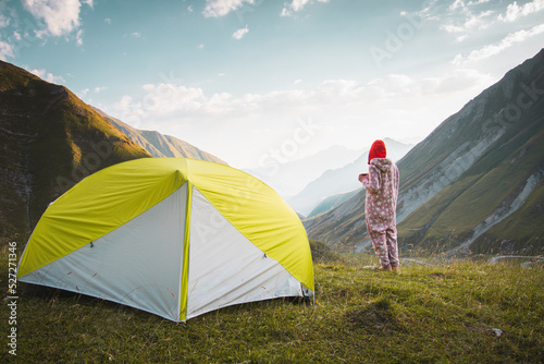 Back view thoughtful female caucasian in pyjamas stand on viewpoint drink fresh coffee in nature enjoy scenic mountains panorama in early morning sunrise alone. photo