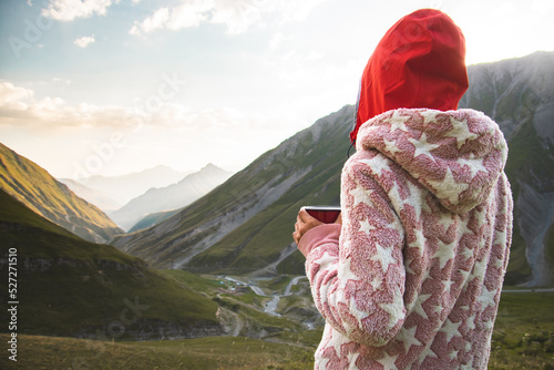 Back view thoughtful female caucasian in pyjamas stand on viewpoint drink fresh coffee in nature enjoy scenic mountains panorama in early morning sunrise alone. photo