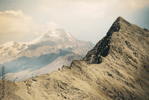 Kazbek peak snowy top surrounded by the mountains in spring time. Dramatic landscapes of Kazbegi national park. Hiking and climbing in caucasus.Deda ena panorama photo