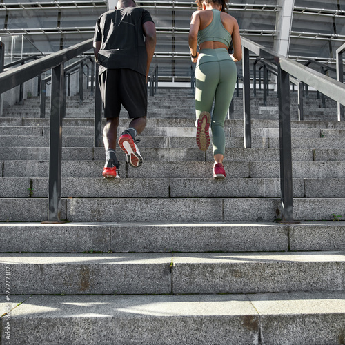 Black sports couple run on staircase near stadium