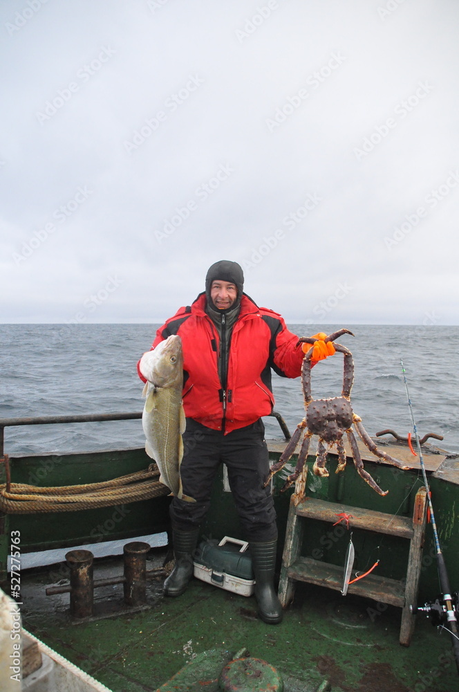 Φωτογραφία Fisherman stands on deck of fishing schooner and holds huge red king crab and bi