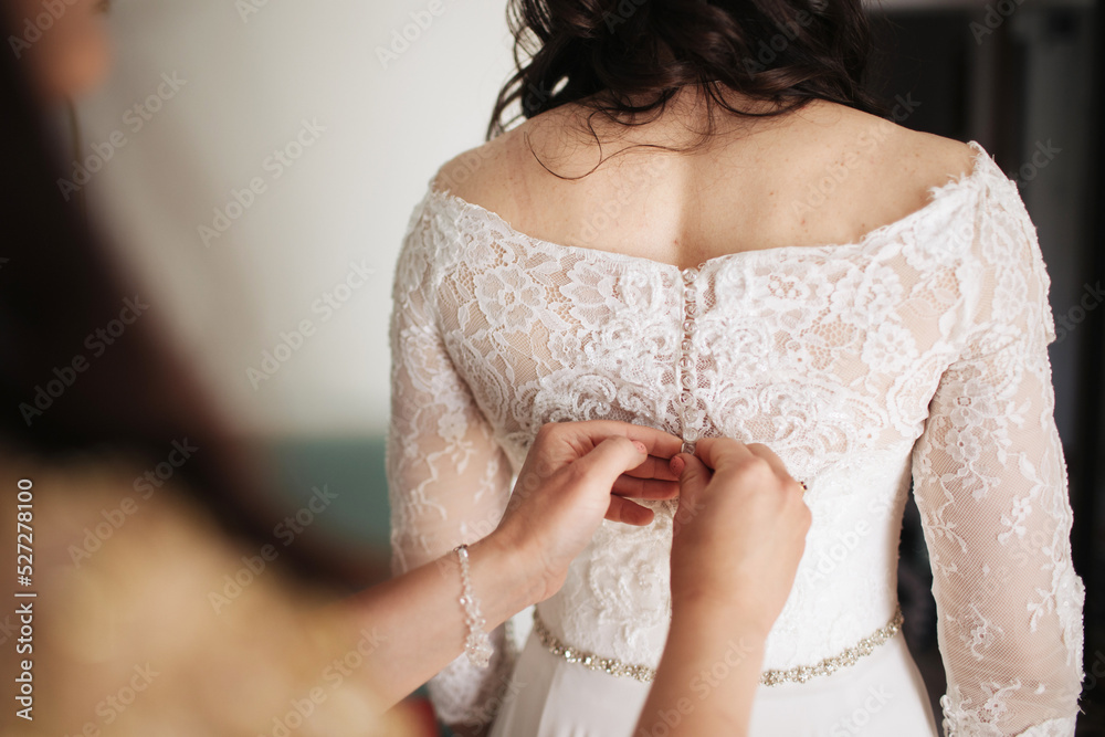 Bride getting ready for the ceremony. Woman dressing up. White wedding dress with buttons. Bridesmaid help background. Wedding preparation. Soon to be wife.