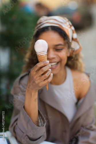 tattooed african american woman in headscarf smiling while holding ice cream cone.