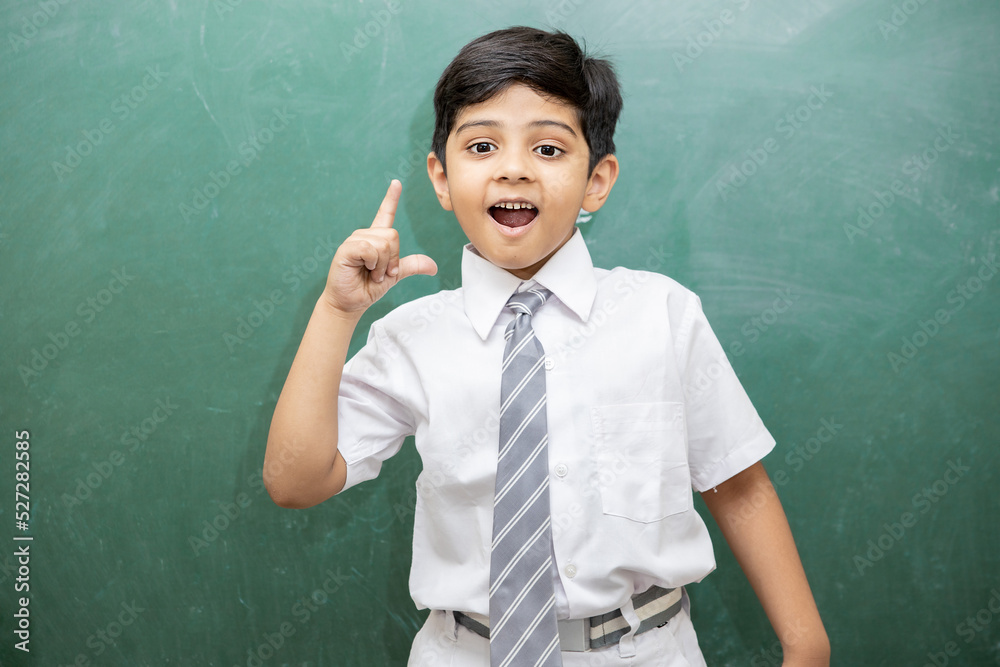 Smart little Indian schoolboy having an idea expression with wide open mouth finally found a solution, blank chalkboard. Education concept.