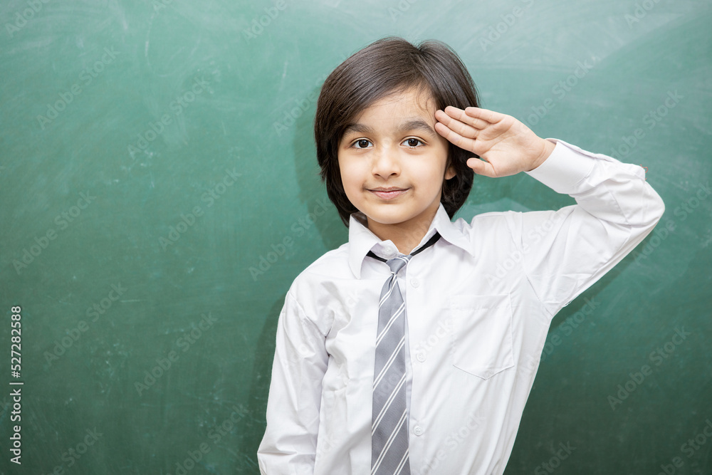 Portrait of happy schoolboy salute due to independence day or republic day while standing against chalkboard, He is wearing school uniform. Portrait of happy schoolboy salute due to independence day or republic day while standing against chalkboard, He is wearing school uniform.