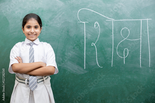 Happy Indian school girl child standing over green chalkboard background with shiksha word writing in hindi. photo