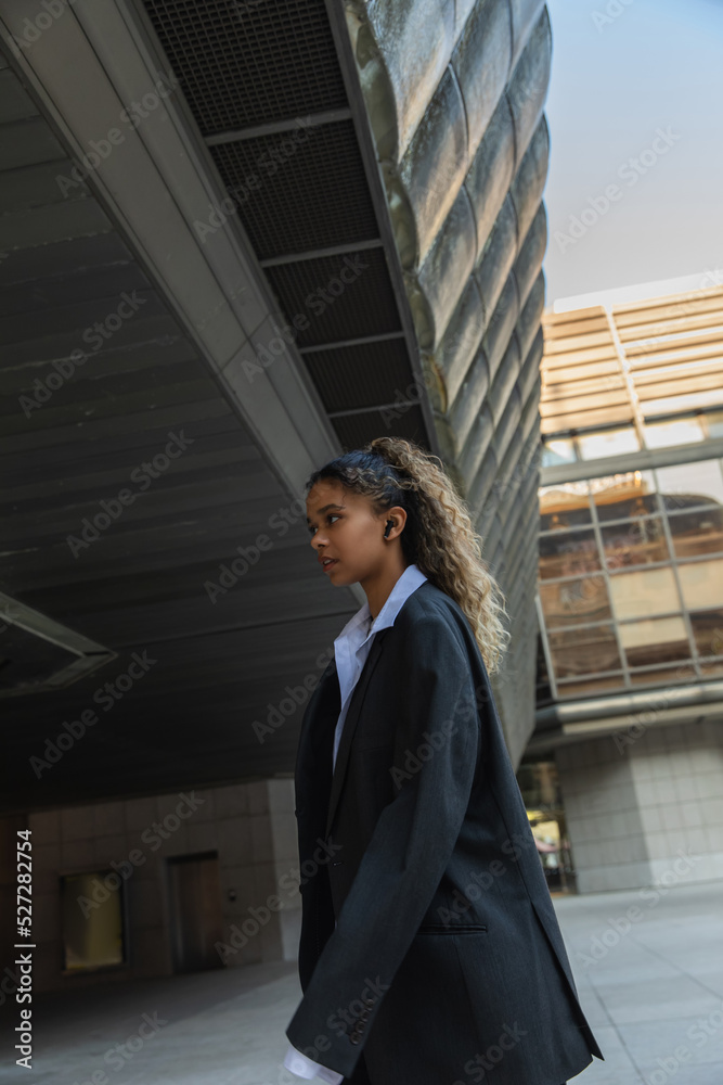 side view of african american woman in oversize suit listening music and walking on urban street in prague. side view of african american woman in oversize suit listening music and walking on urban street in prague.