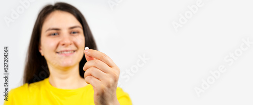 Beautiful healthy brunette woman holding a white pill on a white background with space for text.
