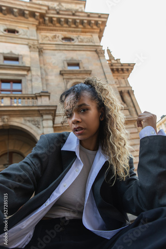 Photography low angle view of african american woman listening music in wireless earphone near national theatre in prague